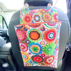 May include: A colorful car trash can with a floral pattern. The trash can hangs from the headrest of a car seat.