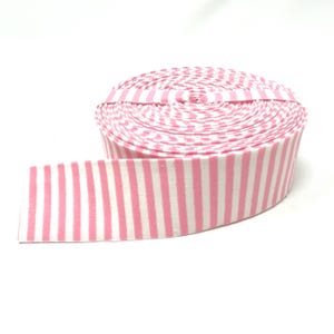 May include: A roll of pink and white striped fabric ribbon. The ribbon is rolled up and the stripes are visible on the outside of the roll.