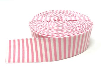 May include: A roll of fabric ribbon featuring a repeating pattern of vertical pink and white stripes. The ribbon is wound into a tight circular spool, with one end extending outward to display the consistent striped design clearly.