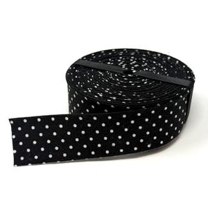 May include: A roll of black fabric ribbon featuring a repeating pattern of small white polka dots. The ribbon is wound into a tight circular spool and secured with a thin black band, with one end of the ribbon extending outward from the main coil.