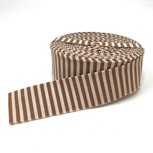 May include: A roll of fabric ribbon featuring a repeating pattern of vertical brown and cream-colored stripes. The ribbon is wound into a tight circular spool, with one end extending outward to display the consistent striped design clearly.