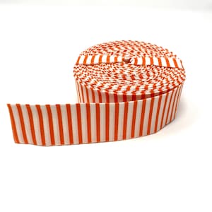 May include: A roll of orange and white striped fabric ribbon. The ribbon is rolled up and the end of the ribbon is laying flat.