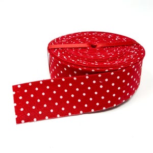 May include: A spool of bright red ribbon featuring a repeating pattern of small white polka dots. The ribbon is wound into a tight circular coil, with one end extending outward to display the fabric texture and the consistent dot pattern.