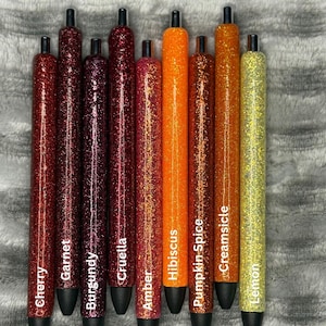 May include: A collection of ten glitter pens in various colors, including red, burgundy, orange, and yellow. Each pen has a black tip and is labeled with a color name such as "Cherry," "Garnet," and "Lemon."