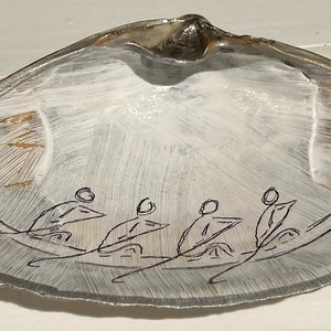 Może przedstawiać: Duża, przezroczysta muszla z białym, malowanym wnętrzem i czarnym rysunkiem liniowym łodzi wiosłowej z czterema postaciami. Muszla ma naturalną, opalizującą krawędź.