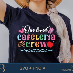 Könnte beinhalten: Ein schwarzes T-Shirt mit dem Text "One loved cafeteria crew" in Regenbogenfarben. Der Text ist von Herzen, Sternen, einem Taco und einem Apfel umgeben.