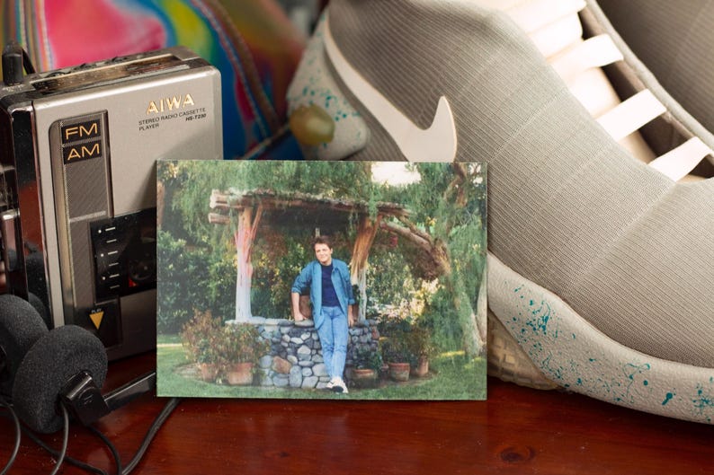 May include: A vintage photograph of a person in denim clothing leaning against a stone structure. A silver AIWA stereo radio cassette player and headphones are on the left. A pair of gray and white Nike sneakers are on the right.