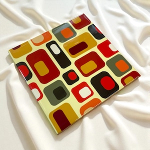 May include: Square decorative tray with a retro geometric pattern. The design features rounded rectangles in red, orange, yellow, brown, green, and white on a light yellow background. The tray is likely made of glass or a similar material.