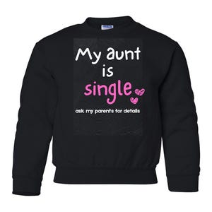 May include: A black long-sleeve sweatshirt featuring a graphic print with white text that reads My aunt is single and pink text that reads single, accompanied by two small pink hearts and the white text ask my parents for details below.