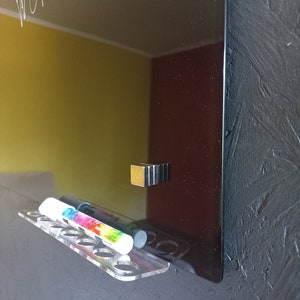 May include: A black glass dry-erase board with the words "the world" written in white. A clear acrylic marker holder with colorful markers is attached to the board. A magnetic holder is also attached to the board.
