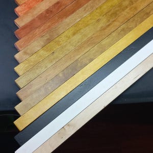 May include: A collection of wooden strips in various shades of brown, yellow, and orange, arranged in a diagonal pattern. The strips are painted in different colors, including black and white.