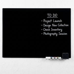 May include: A black rectangular whiteboard with the words "TO DO" and a list of tasks in white. The tasks include "Project Launch", "Design New Collection", "Check Inventory", and "Photography Session". A small eraser and marker holder are at the bottom.