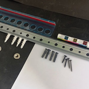 May include: Hardware kit with a metal rail, screws, wall anchors, and a white marker. Includes a clear plastic bag with a red seal and metal washers. The rail has evenly spaced holes for mounting.