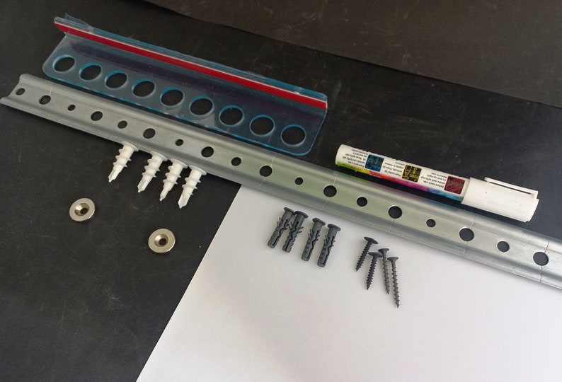 May include: Hardware kit with a metal rail, screws, wall anchors, and a white marker. Includes a clear plastic bag with a red seal and metal washers. The rail has evenly spaced holes for mounting.