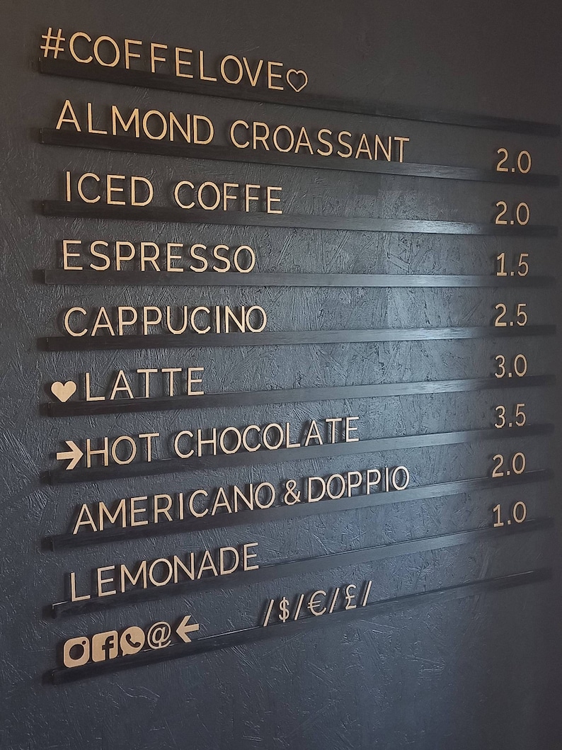 May include: Black chalkboard menu with gold lettering listing coffee and beverage options with prices. The menu includes almond croissant, iced coffee, espresso, cappuccino, latte, hot chocolate, Americano & Doppio, lemonade, and the text #COFFELOVE♡, /$/&euro;/&pound;/, and OFO@.