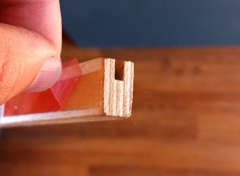 May include: Close-up of a wooden piece with a U-shaped cutout. The wood is light brown and has a natural grain. A piece of red tape is visible on the top of the wood.