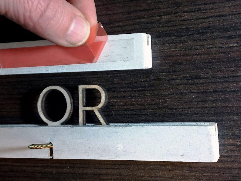 May include: Close-up of the word "OR" made of wood letters. The letters are attached to a white surface with a red adhesive strip.