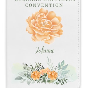 May include: White journal with the text "2026 ETERNAL HAPPINESS CONVENTION" in green. The journal features an orange floral design and the name "Johnna" in script. A floral arrangement with orange flowers and green leaves is at the bottom.