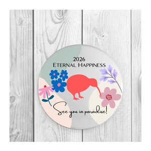 Puede incluir: Un adorno circular con la silueta de un ave kiwi roja rodeada de ilustraciones florales azules y rosas. El texto dice 2026 ETERNAL HAPPINESS y See you in paradise! sobre un fondo de formas en tonos pastel suaves como salvia, crema y blanco.