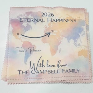 Op de afbeelding: Een vierkante stof met een wereldkaartontwerp. De kaart toont een route van Texas naar Roemenië, met de tekst "2026 Eternal Happiness" en "With love from THE CAMPBELL FAMILY."