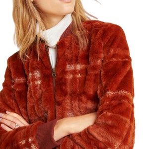 May include: A rust-colored faux fur bomber jacket with a plaid pattern. The jacket has a zipper closure and ribbed cuffs and hem.