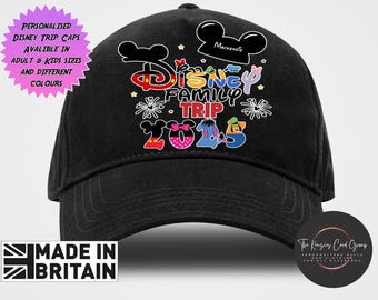 Może przedstawiać: Czarna czapka z daszkiem z kolorowym nadrukiem graficznym z napisem Disney Family Trip 2025. Wzór zawiera stylizowane uszy postaci, małe gwiazdki i fajerwerki. Czarna ikona w kształcie ucha u góry zawiera imię Mackenzie.