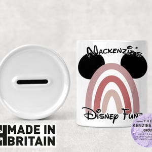 May include: White ceramic piggy bank with a slot on top. The piggy bank is decorated with a rainbow and Mickey Mouse ears. The text "Mackenzie's Disney Fund" is printed on the front.