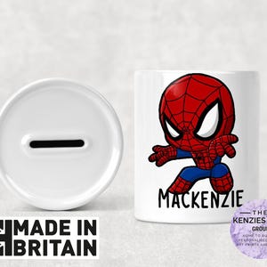 May include: A white ceramic money box with a slot, next to a matching mug featuring a cartoon Spider-Man design in red, blue, and black. The name "Mackenzie" is printed below the character. The words "MADE IN BRITAIN" are also visible.