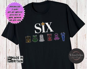 May include: A black short-sleeved t-shirt featuring the white text SIX with a small gold crown above the letter I. Below the text are six colorful illustrations of historical-style dresses in gold, green, silver, red, purple, and blue.