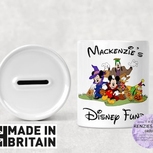 May include: White ceramic piggy bank with a slot on top. The front of the bank features a colorful illustration of Mickey Mouse and friends dressed in Halloween costumes. The text "Mackenzie's Disney Fun" is printed on the bank.