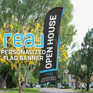 May include: A black and blue open house flag banner with the text "OPEN HOUSE" in white. The banner is attached to a pole and is standing in front of a green lawn with trees and houses in the background. The text "[real]" is printed on the bottom of the banner, along with the text "Julie Kitchens 562-567-SOLD".