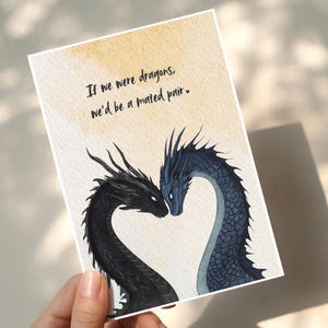 Op de afbeelding: Wenskaart met een drakenillustratie. Twee draken, &eacute;&eacute;n zwart en &eacute;&eacute;n blauw, vormen een hart. De tekst luidt: "Als we draken waren, zouden we een gepaard paar zijn."