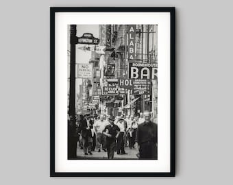 May include: A black and white photograph of a city street scene with people walking past various storefronts. The storefronts have signs with text that reads "RIVINGTON ST", "ONE-WAY", "NO PARKING", "FIXTURE", "ALABA", "ROUNDHOUSE BAR", "HOU", "KAL STAI H CLOTHIN CO GENERAL METHANE SE", "BAKEMIS STORE FIXTU ES", and "217".
