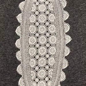 May include: White crocheted oval table runner with a delicate floral pattern. The runner has a scalloped edge and is made of fine thread.