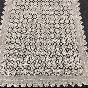 May include: White crocheted tablecloth with a delicate circular pattern. The tablecloth has a scalloped edge.