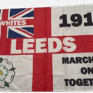 Puede incluir: Una bandera blanca con una cruz roja y una rosa blanca. La bandera también tiene el texto "The Whites", "Leeds", "1919", "Marching On Together" en letras negras.