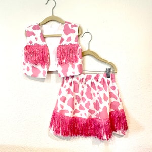 Pink and white cowhide print cowgirl costume with pink rhinestones and pink sequin fringe.