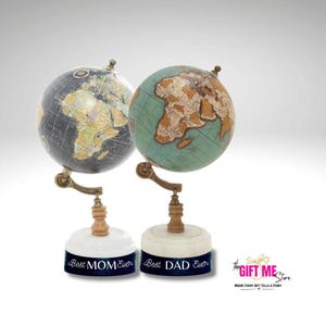 May include: Two decorative globes with an antique appearance. One globe is dark with a world map, the other is teal with a map. Each globe sits on a white base with a dark blue band that reads "Best MOM Ever" and "Best DAD Ever".