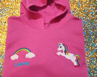May include: Pink hooded sweatshirt with a rainbow and a unicorn embroidered on the front. The name "Lauren" is embroidered below the rainbow.