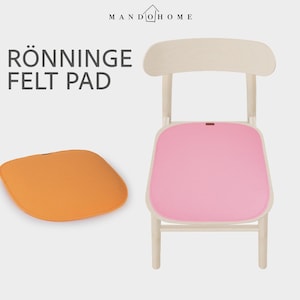 May include: A light wood chair with a pink felt pad on the seat and a separate orange felt pad placed to the left. The text MANDO HOME and RÖNNINGE FELT PAD are visible at the top. The pads have a rounded square shape and a small brown tag.