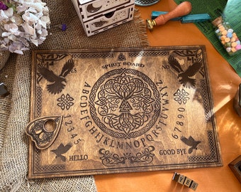 May include: Wooden spirit board with a Celtic knot design and a tree of life in the center. The board has letters, numbers, and the words "yes", "no", "hello", and "good bye" printed on it. A planchette is included.