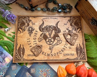 May include: Wooden spirit board with a pentagram and a skull design. The board has a planchette and the letters of the alphabet, numbers 1-9, and the words "yes", "no", "hello", and "good bye".