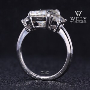 May include: A silver ring with three large, clear, emerald-cut gemstones. The ring is set on a plain band.