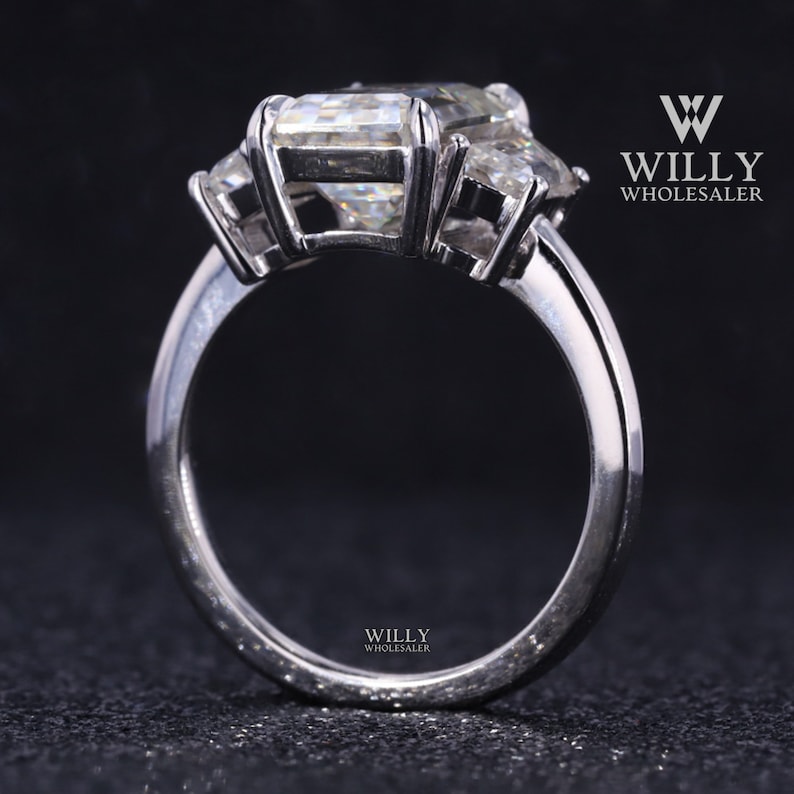 May include: A silver ring with three large, clear, emerald-cut gemstones. The ring is set on a plain band.