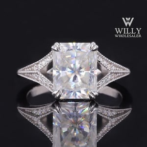 May include: A silver ring featuring a large, clear, square-shaped gemstone. The ring has a delicate, intricate design with small diamonds set in the band.