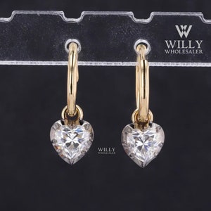 Op de afbeelding: Een paar gouden creolen met een hangende hartvormige diamant hanger. De oorbellen zijn op een witte displaystandaard.