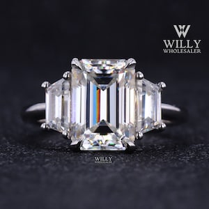 May include: A silver ring with a large emerald-cut diamond center stone and two smaller baguette-cut diamonds on either side.