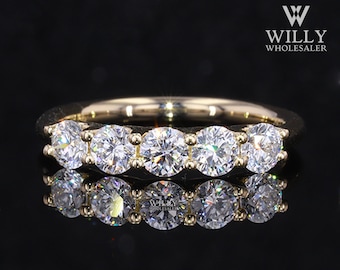 May include: A gold band with five round, clear gemstones. The band is reflecting light, creating a rainbow effect.