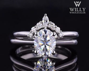 May include: A silver engagement ring set with a large oval-shaped center stone and a delicate crown of smaller stones. The ring is set on a black background.
