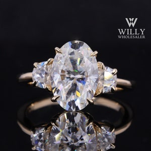 May include: A gold ring featuring a large oval-shaped centre stone and two smaller oval-shaped stones on either side. The ring is set against a black background.